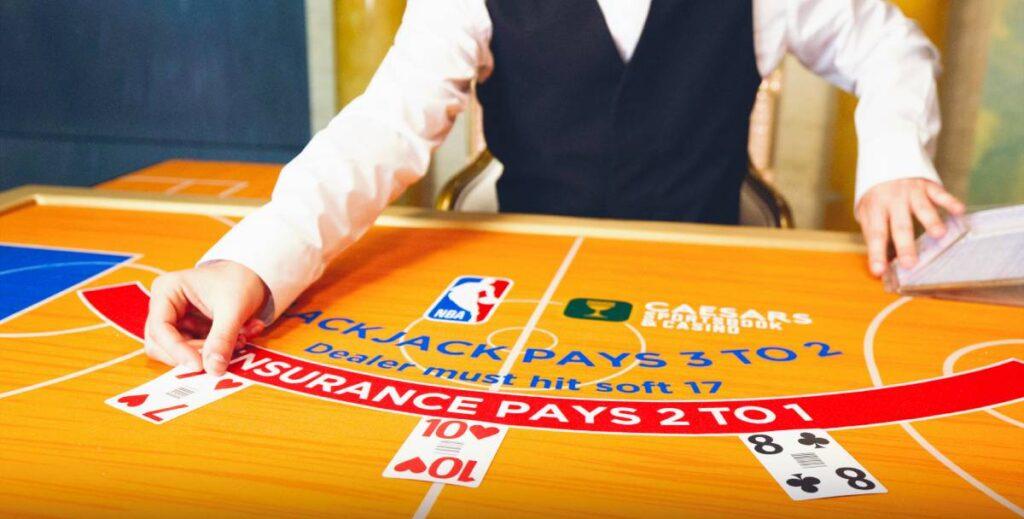 Stůl NBA Blackjack v kasinu Caesars s logem NBA a designem basketbalového hřiště. Dealer rozdává karty ve stylu playoff.